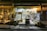 A well-lit store with a large variety of products displayed on shelves both inside and outside. The store's signage reads 'Amalthia's' and offers a range of food, drinks, beauty products, and other items. There are hanging lamps and potted plants near the entrance, contributing to a welcoming atmosphere.