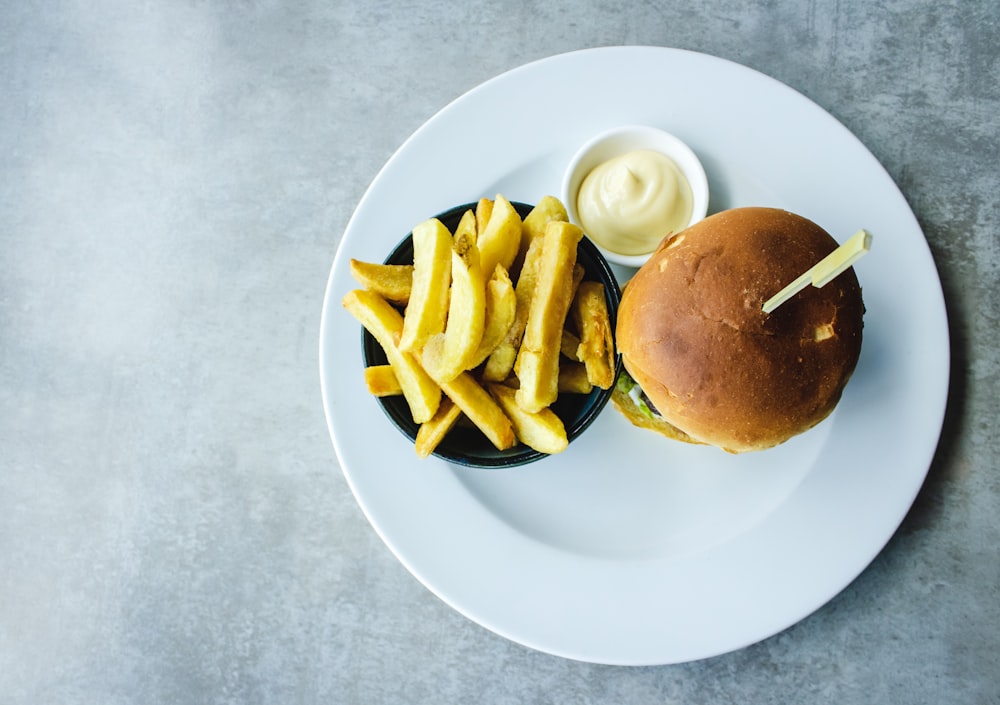 Plato de papas fritas junto a hamburguesa servido en plato blanco