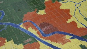 A tiled floor map features different colored sections with blue lines representing rivers or roads. The colorful sections are labeled with names, including 'SEVILLA' and 'CAMAS'.
