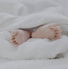 barefooted baby covering white blanket