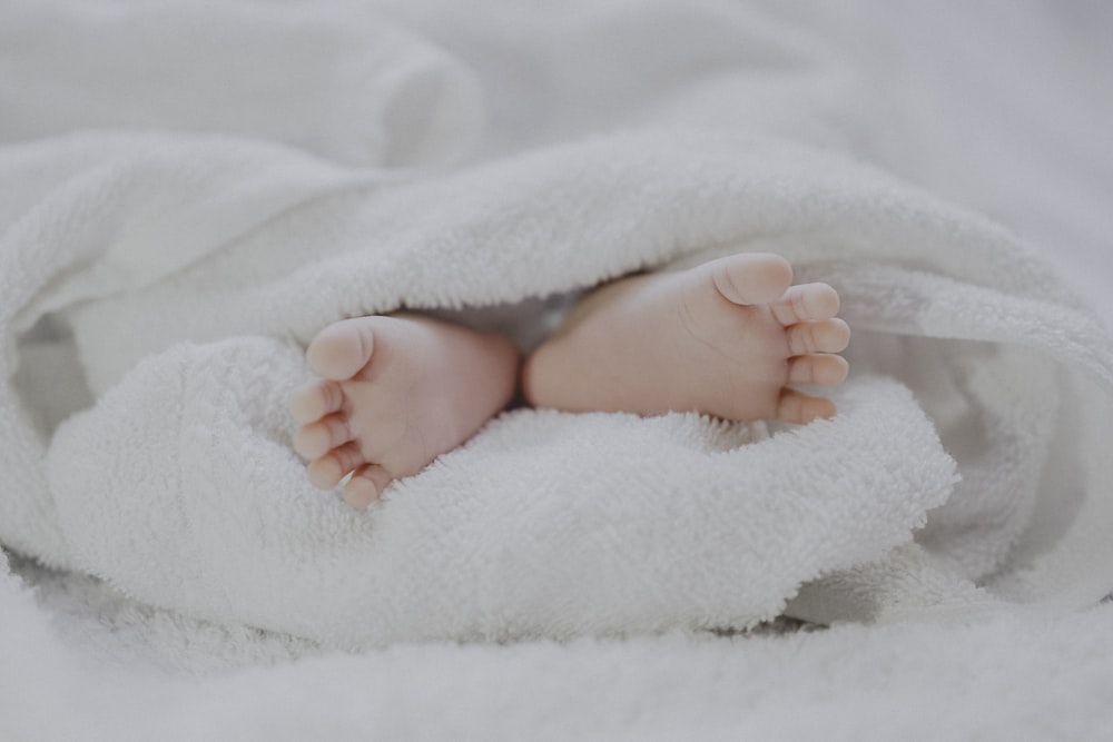 barefooted baby covering white blanket