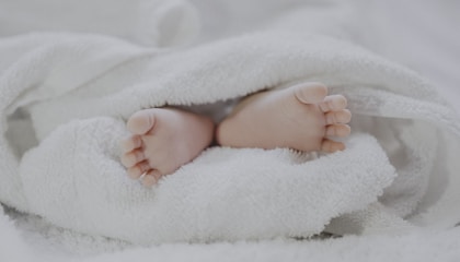 barefooted baby covering white blanket