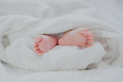 barefooted baby covering white blanket baby teams background