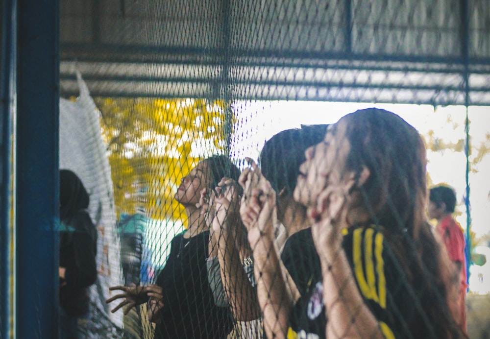 people leaning on wire fence