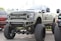 A large, heavily modified pickup truck with an elevated suspension and oversized tires. The truck features custom bumpers, a distinctive grille with a star emblem, and multiple light bars. The body is painted in a matte military green color.