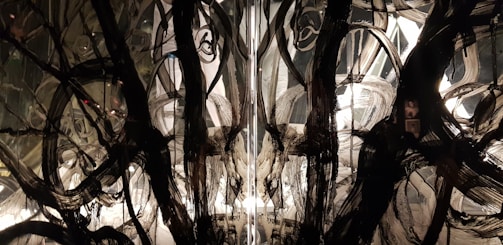 Intricate abstract patterns featuring swirling black brushstrokes and broad strokes of white on a reflective surface. The design creates a dramatic contrast and evokes a sense of depth and complexity.