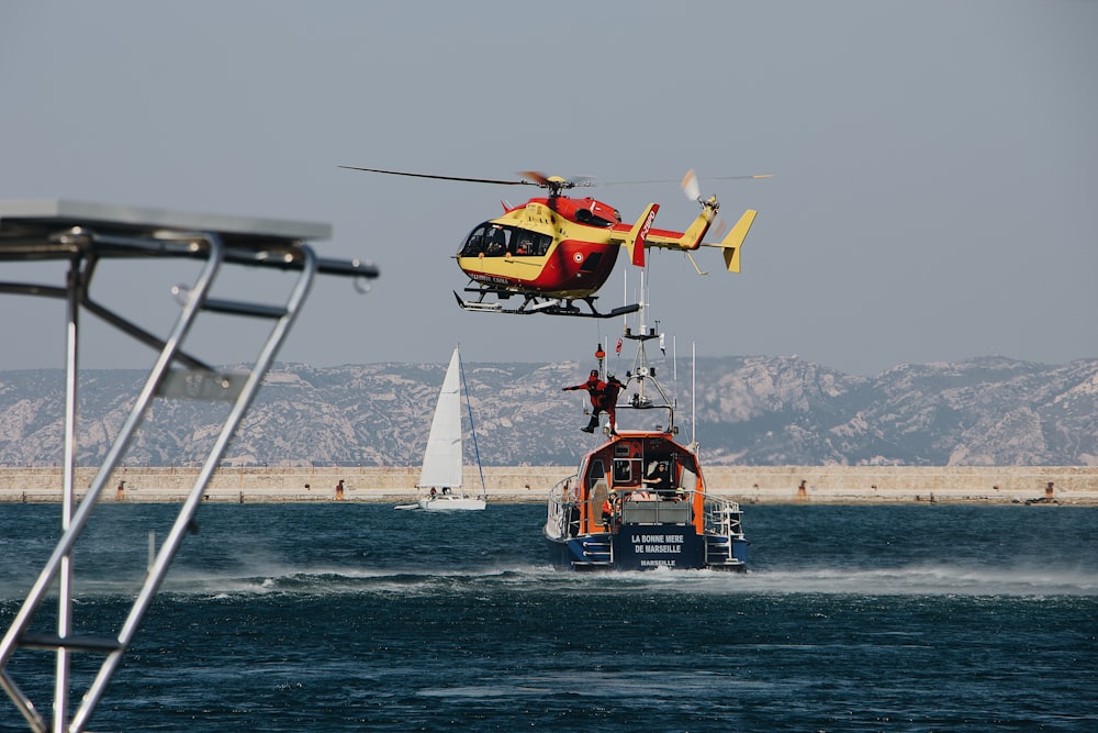 red and yellow helicopter flying above sea during daytime