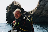 A smiling dive instructor adjusts gear on a bright coral reef backdrop.