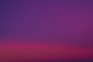 a purple and pink sky with a plane in the distance