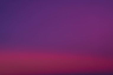 a purple and pink sky with a plane in the distance