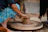 A joyful Indian woman shaping clay on a pottery wheel in a sunlit studio surrounded by art supplies.