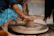 A joyful Indian woman shaping clay on a pottery wheel in a sunlit studio surrounded by art supplies.