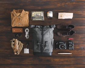 A flat lay of survival gear, inspirational pictures, and custom design shirts arranged on a wooden surface.