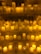 Numerous lit candles of varying heights are organized on several shelves, with wax dripping down the sides, creating an ambient and warm glow.