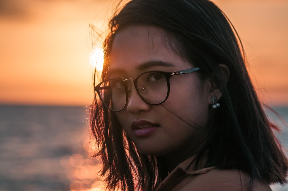 woman wearing black framed sunglasses at beach during sunset
