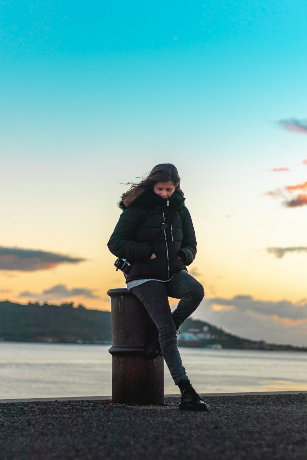 woman leaning against metal post by the sea