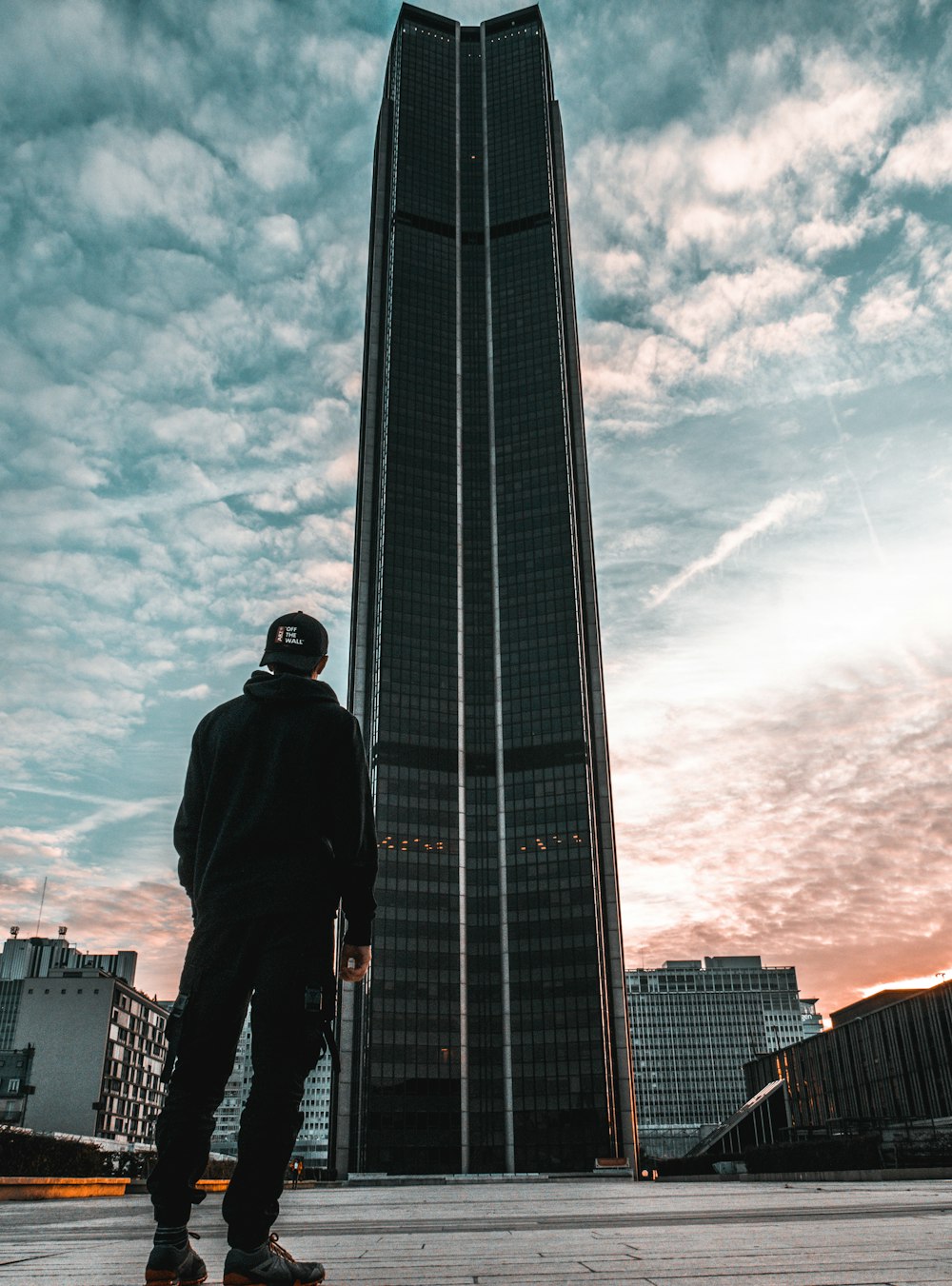 hombre con gorra, chaqueta y pantalones negros mirando en un edificio de gran altura