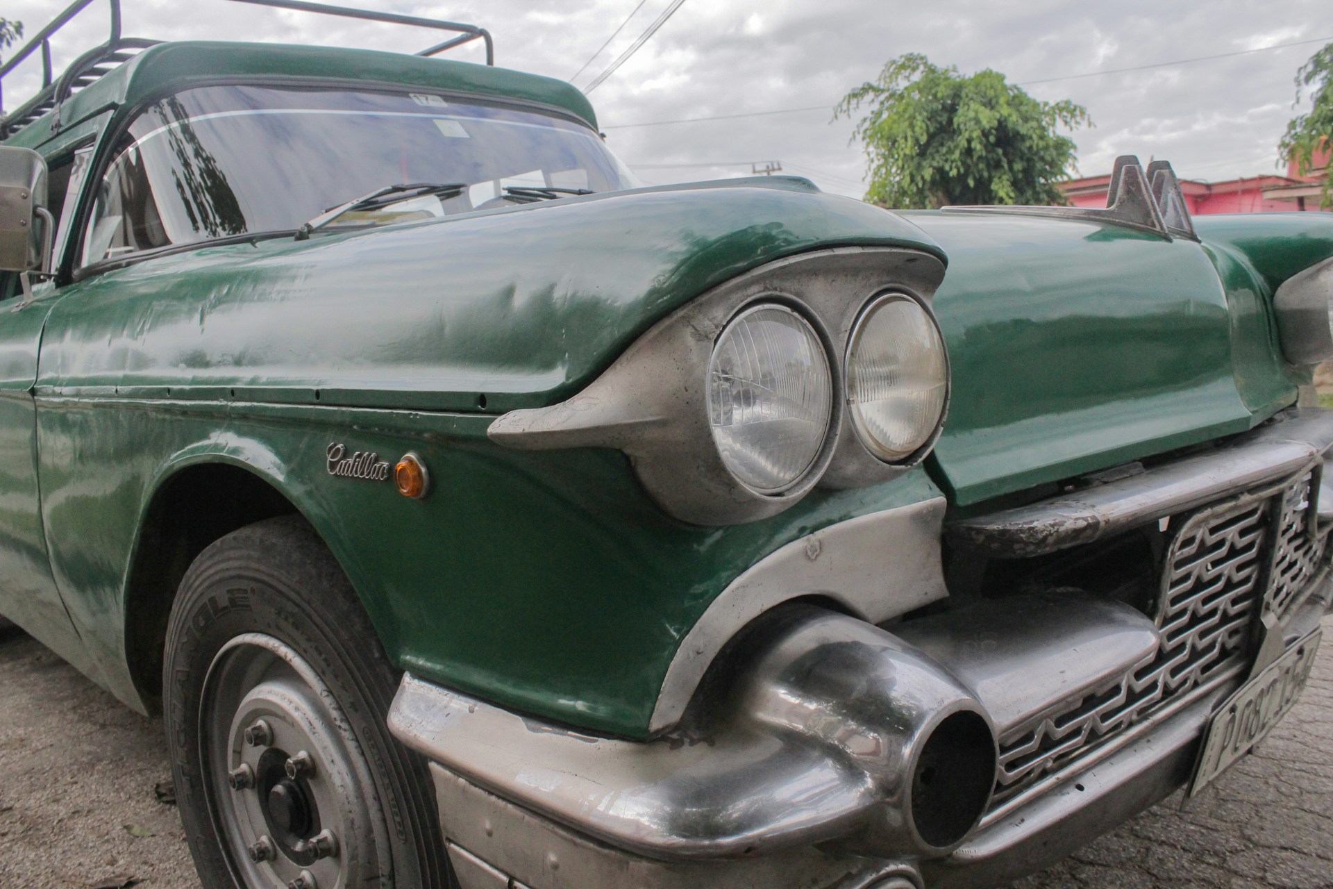 A close-up view of a classic car, featuring large round headlights and a distinctive vintage grille, with a glossy green paint job. The front and side of the vehicle are visible, showing metal detailing and an older style license plate.