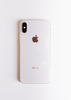 A white smartphone with a dual camera setup on the top left corner and an Apple logo in the center, placed on a plain white background. The device is sleek and modern in design.