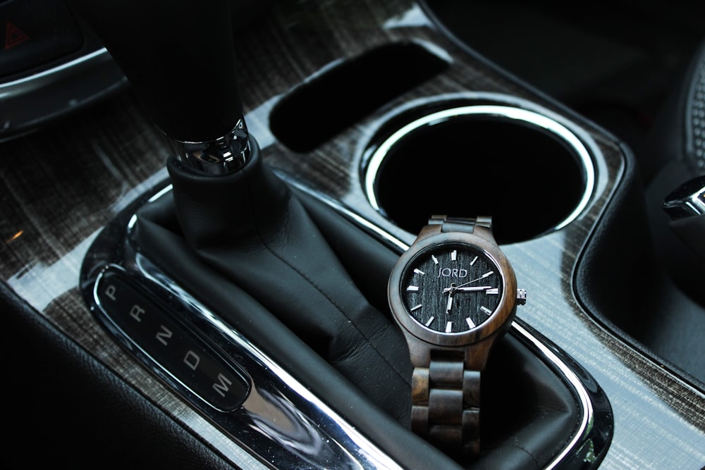 round gold-colored analog watch near the vehicle gear lever