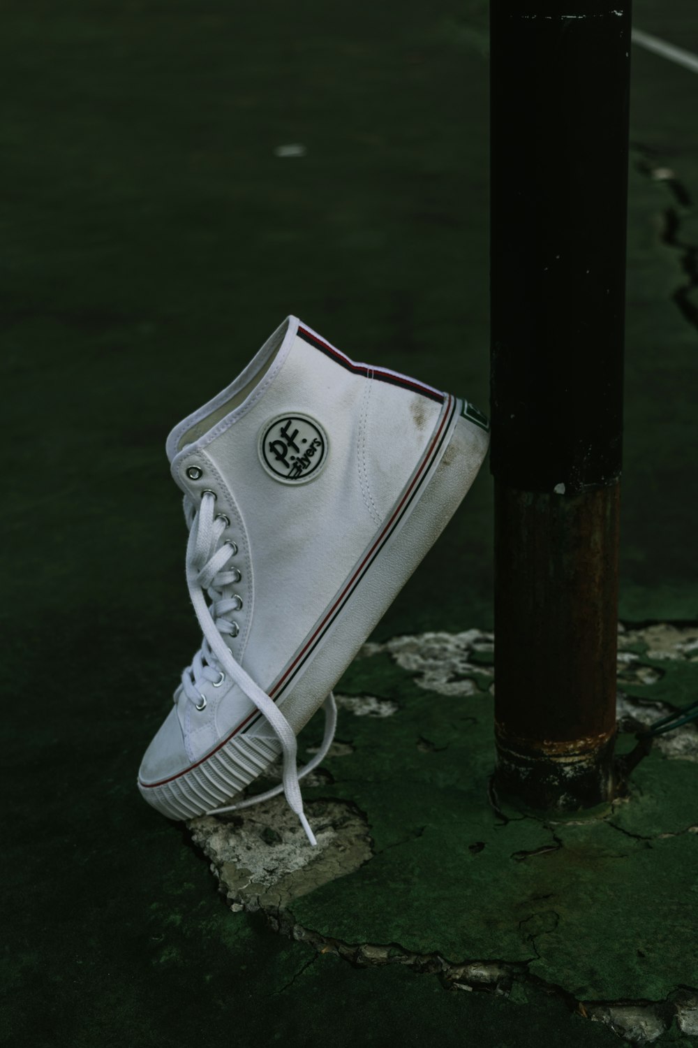 unpaired white PF high-top sneaker leaning on black post