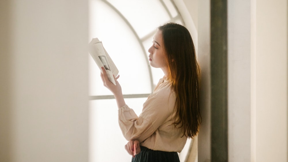 woman leaning on the wall while reading book