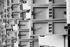 A series of open mailboxes are aligned in a repeating pattern, with barcodes visible on the inside of some doors. The scene is captured in black and white, emphasizing the metal texture and geometrical design.