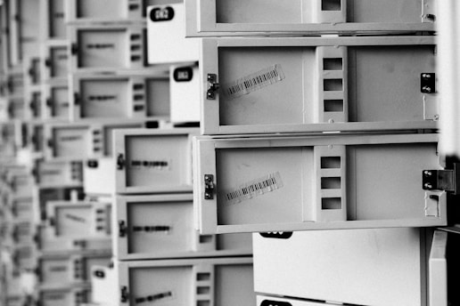 A series of open mailboxes are aligned in a repeating pattern, with barcodes visible on the inside of some doors. The scene is captured in black and white, emphasizing the metal texture and geometrical design.