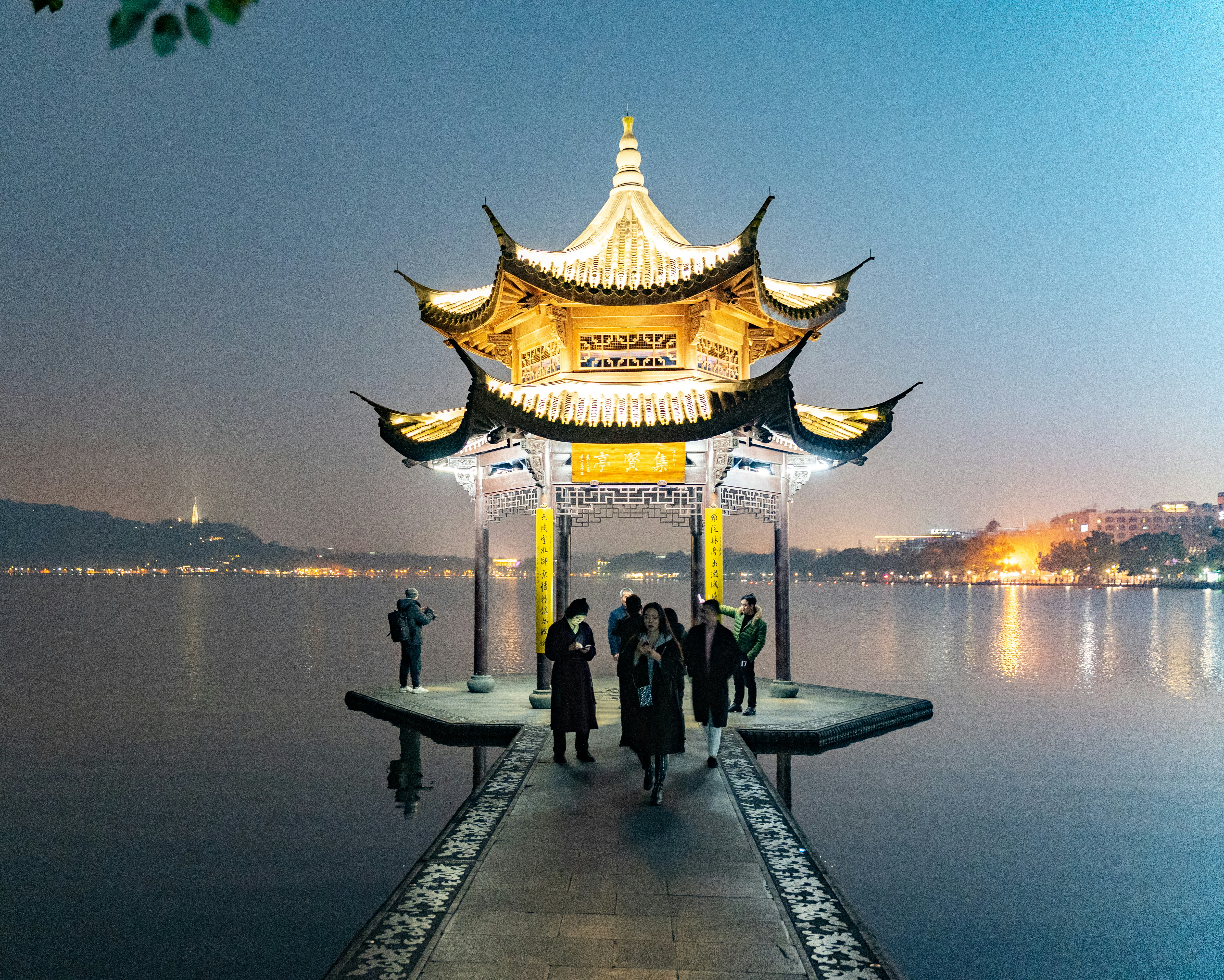 group of people on dock during golden hour, Another night shot on West Lake, Hangzhou. Blue Hue is from a large commercial screen that