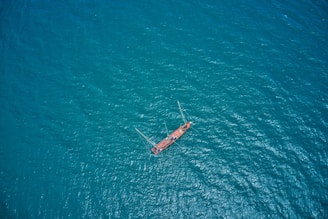 Aerial view of a solitary red sailboat sailing on a vast expanse of blue ocean water, creating a sense of isolation and adventure.