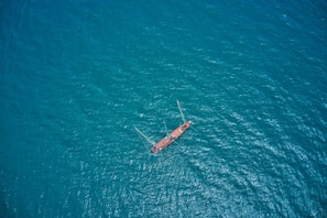 Aerial view of a solitary red sailboat sailing on a vast expanse of blue ocean water, creating a sense of isolation and adventure.