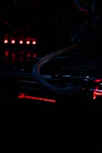 A close-up view of a computer component with illuminated red lights, featuring the text 'Republic of Gamers.' The environment is dark, highlighting the glowing lights and intricate wiring.