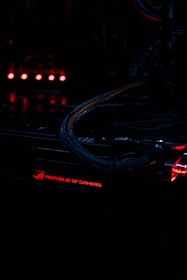 A close-up view of a computer component with illuminated red lights, featuring the text 'Republic of Gamers.' The environment is dark, highlighting the glowing lights and intricate wiring.