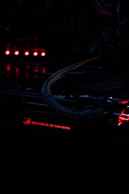 A close-up view of a computer component with illuminated red lights, featuring the text 'Republic of Gamers.' The environment is dark, highlighting the glowing lights and intricate wiring.