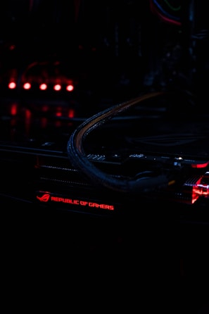 A close-up view of a computer component with illuminated red lights, featuring the text 'Republic of Gamers.' The environment is dark, highlighting the glowing lights and intricate wiring.