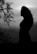 A silhouette of a person with long curly hair standing against a cloudy sky backdrop. Bare branches of a tree are visible in the foreground, adding texture to the scene.