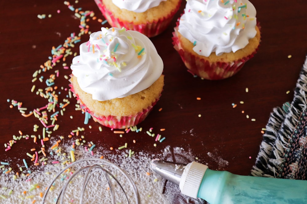 three cupcakes with white frosting and sprinkles