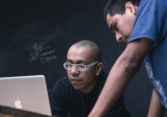 two men watching on silver MacBook