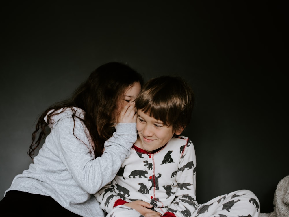 girl in gray jacket whispering on boy's right ear