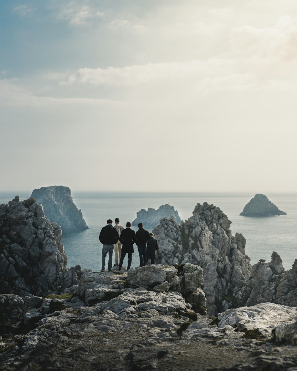 cinq personnes debout sur une colline rocheuse regardant la mer calme