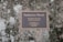 A memorial plaque mounted on a natural stone surface, inscribed with a dedication to Santacroce Woods, urging kindness to the Earth and its creatures.