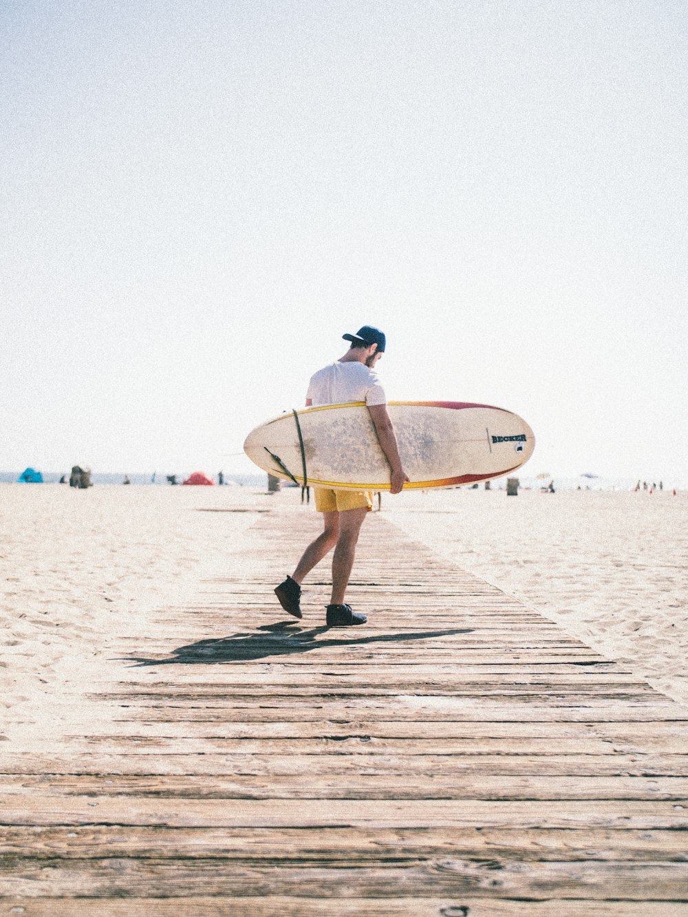 man carrying surfboard while walking on wooden pathway