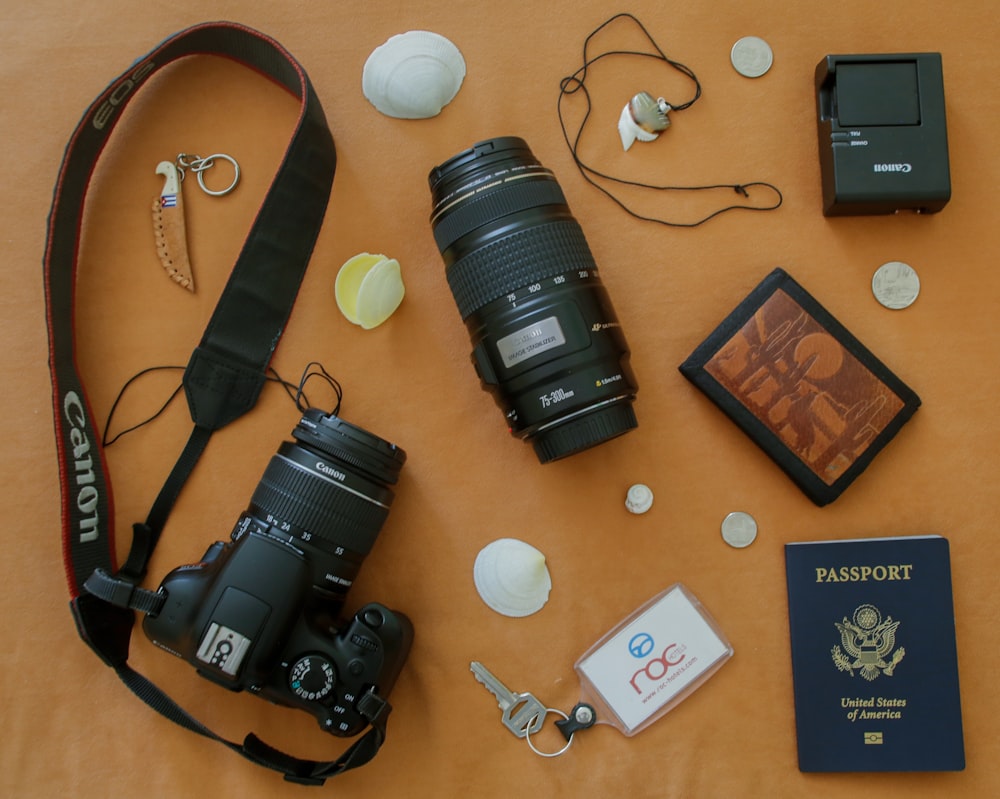 Fotocamera Canon DLSR nera con obiettivo, chiavi, portafoglio, caricabatterie e passaporto