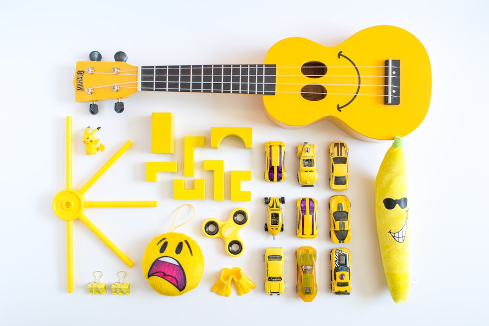 ukulele amarelo, carros, brinquedo de pelúcia emoji na superfície branca