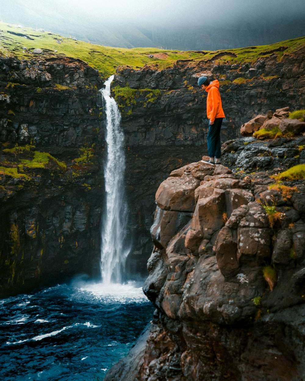 person standing on rock formation watching waterfall during daytime