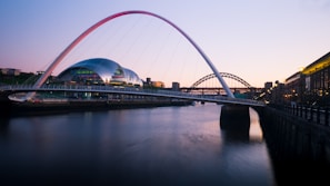 A sleek modern bridge arching gracefully over a river at sunset.