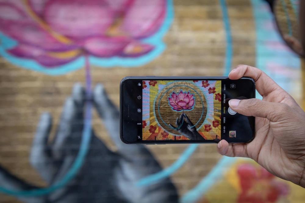 person taking picture of flower painting on wall