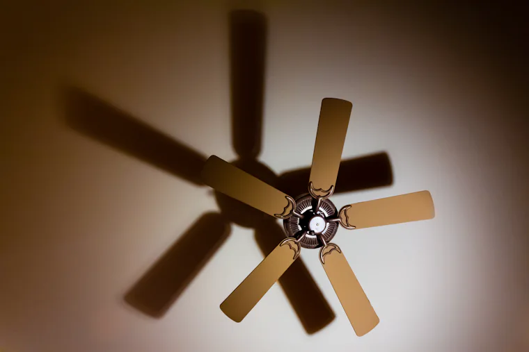 Shadow of a five-blade ceiling fan cast on a ceiling