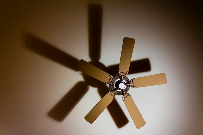 Ventilador de techo de cinco aspas girando, con su sombra proyectada en el cielorraso