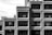 Concrete brutalist building with a uniform grid of rectangular windows. The structure features an industrial and geometric design, casting strong shadows due to the angle of sunlight. The visible portion of the building is composed of repetitive patterns and forms.